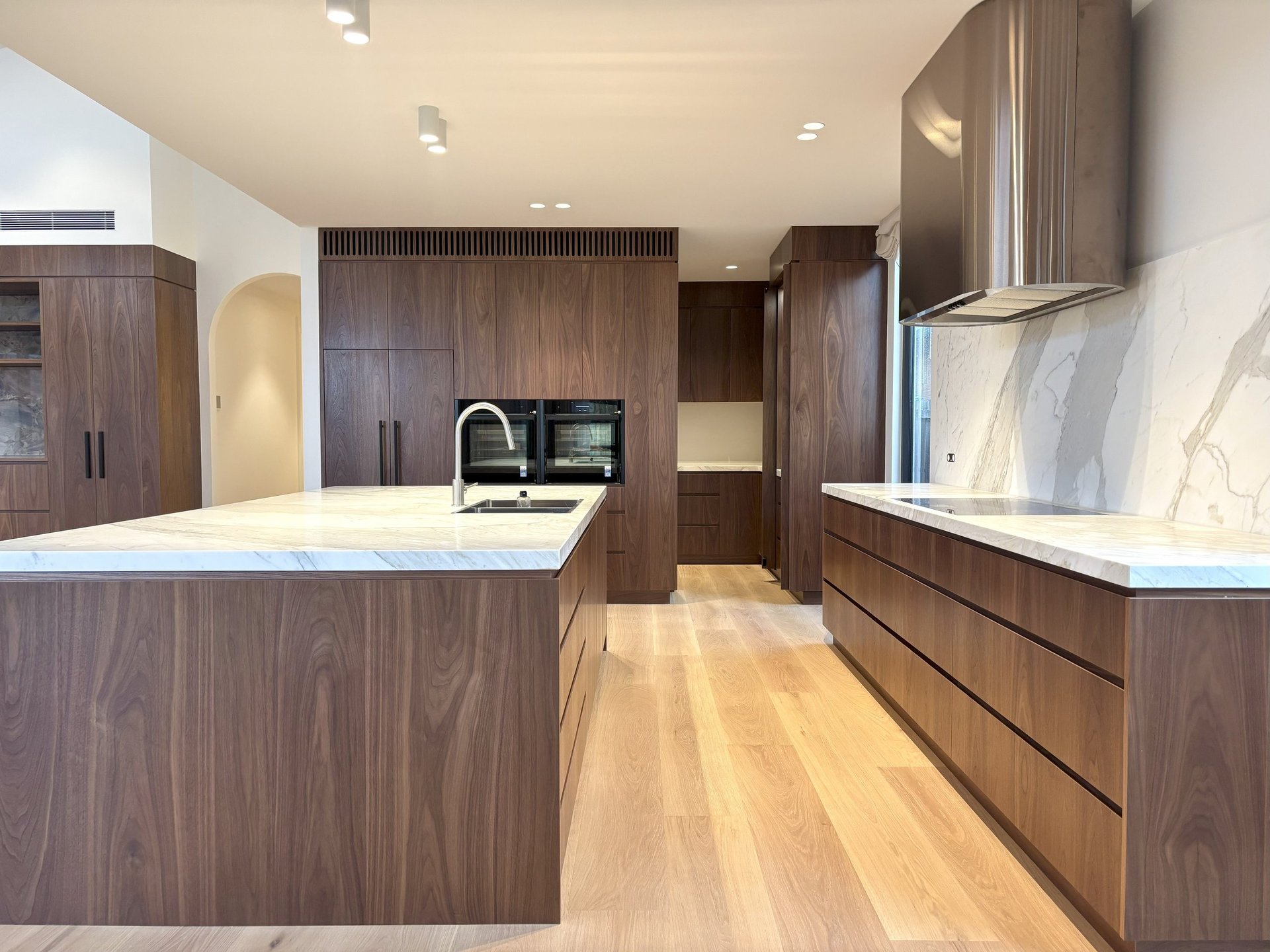 Modern kitchen with dark wood cabinetry, white marble countertops, island with seating, and light wood flooring