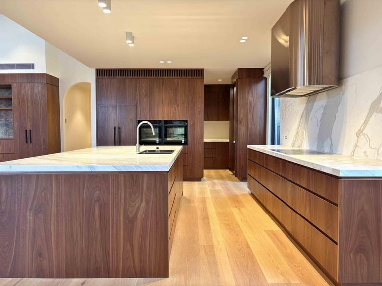 Modern kitchen with dark wood cabinetry, white marble countertops, island, and wooden flooring
